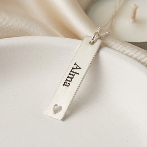 Silver rectangular pendant necklace engraved with Allura and a small heart, displayed on white fabric