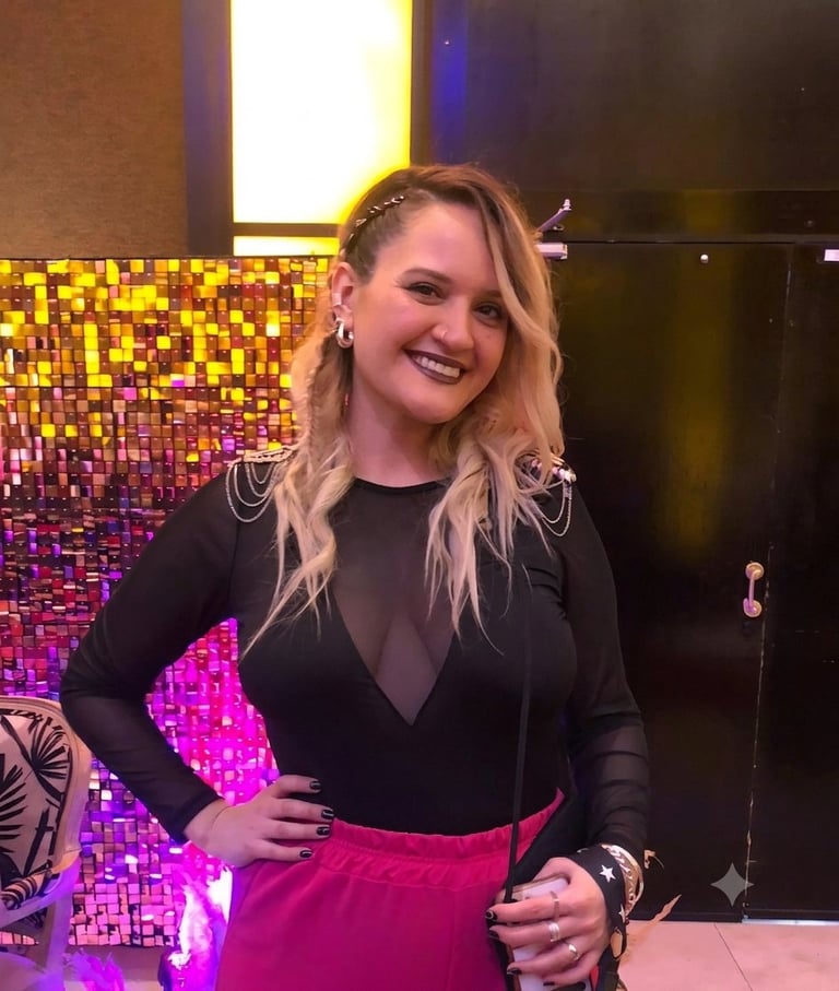 Woman smiling at nightclub with long blonde hair, black top, and pink skirt, standing against colorful pixelated backdrop